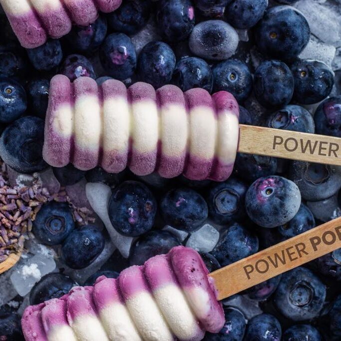 blueberry yogurt pops with a powerpops stick on top of frozen blueberries and ice with lavender